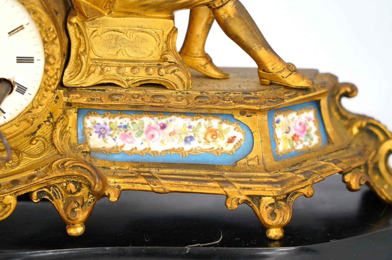 A 19th century figurative ormolu mantel clock, with floral porcelain panels, on stand with key and pendulum, stand approximately 39cm wide. Condition - clock dial cracked, clock untested as working